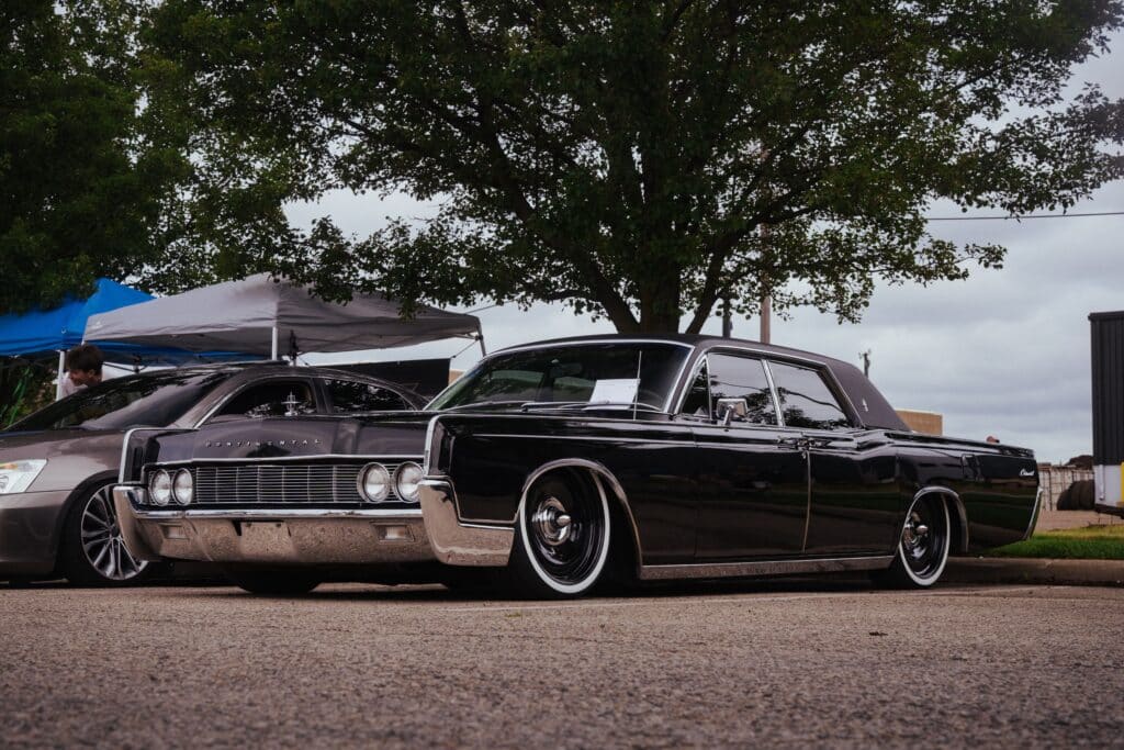 Vintage Lincoln Continental showcased in an outdoor car exhibition, under trees.