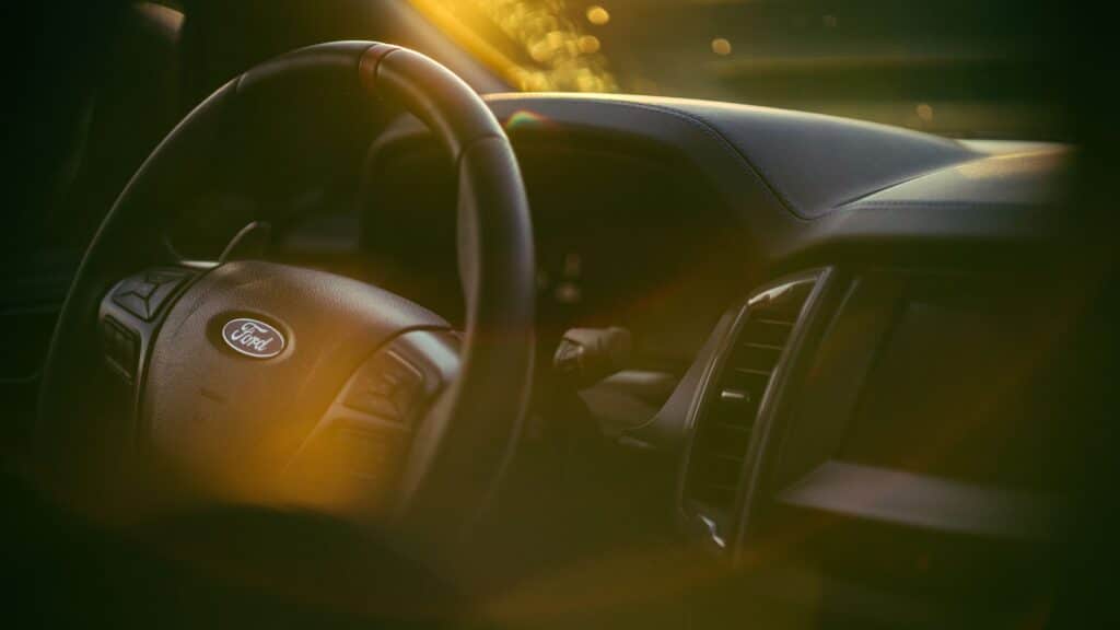 Ford steering wheel close-up under warm sunlight highlighting interior design.