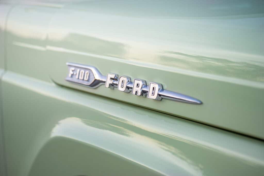 Close-up view of a vintage Ford F-100 emblem on a pastel green vehicle, ideal for automotive enthusiasts.