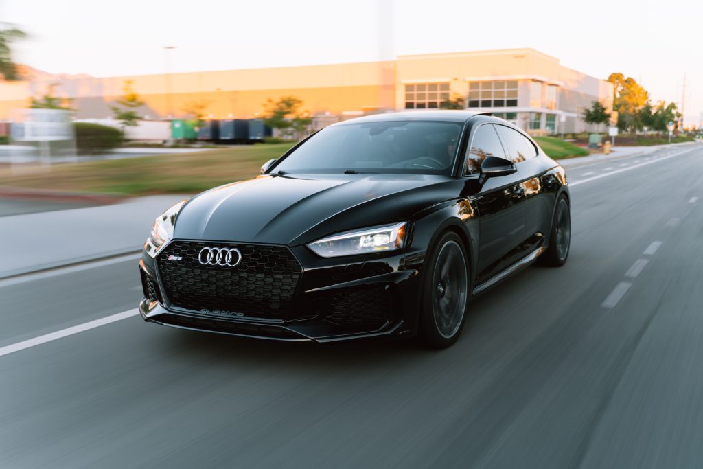 A sleek black Audi RS5 in motion on a city road during daytime.