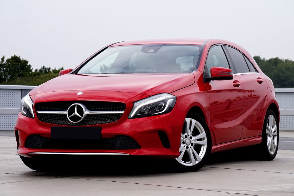Sleek red luxury sedan with chrome details, parked outdoors on a concrete lot.