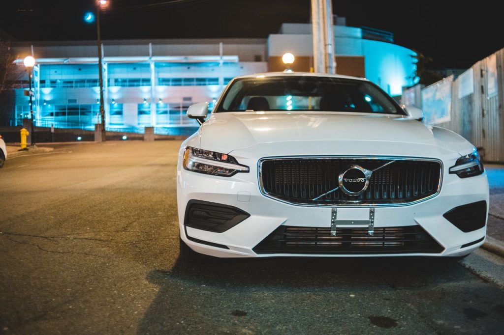 Front view of a white Volvo car parked on the roadside at night under urban lights.